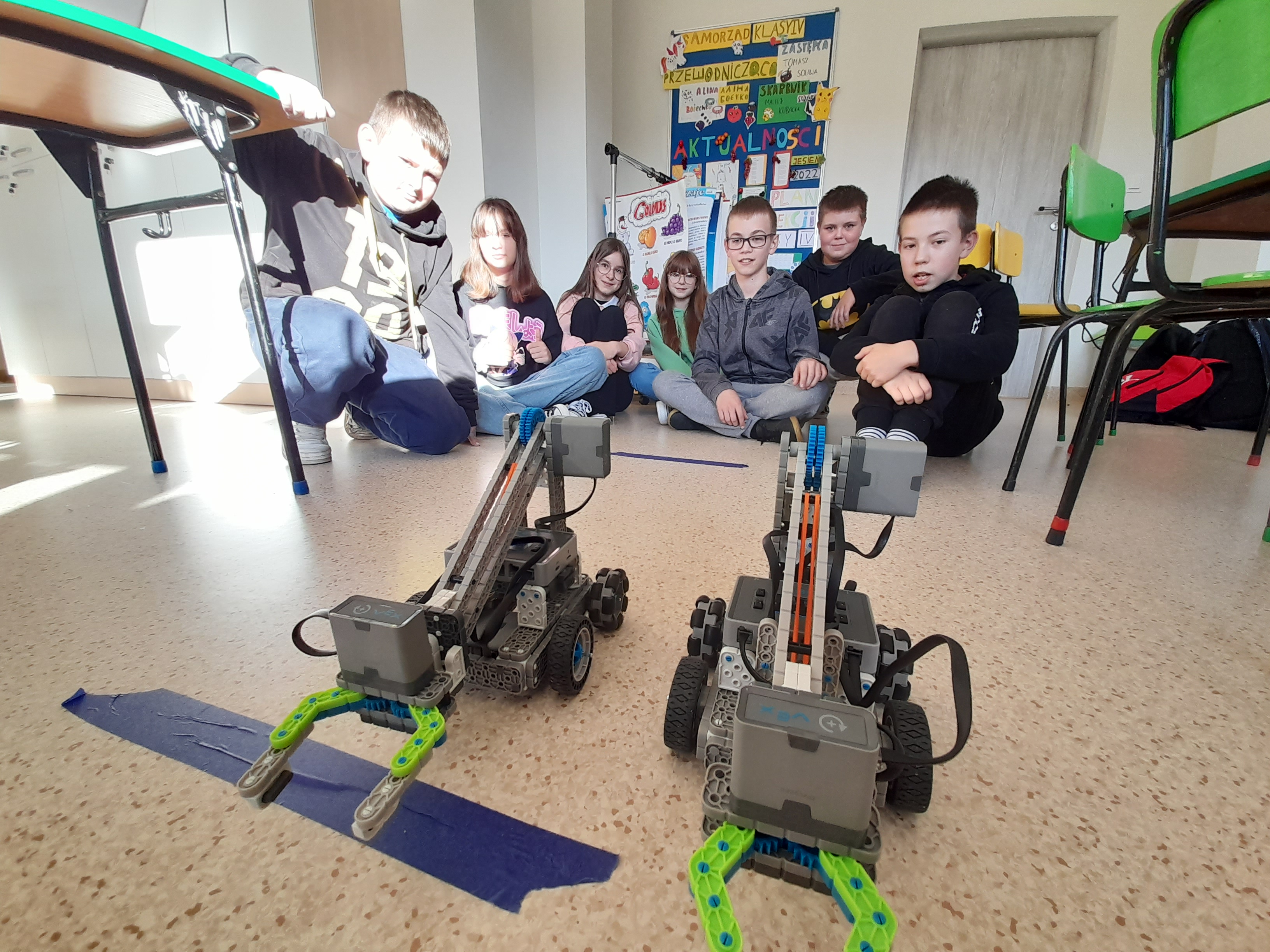 Zdjęcie przedstawia uczniów podziwiających swoje zaprogramowane roboty.