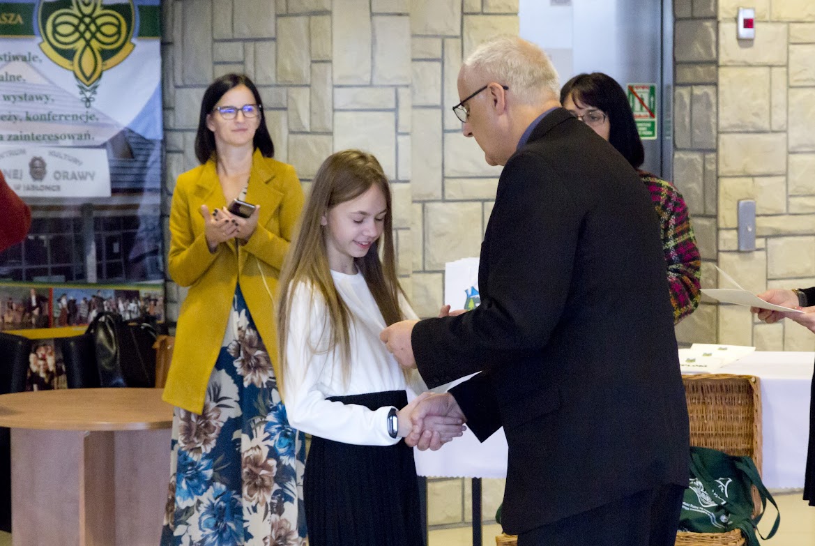 Zdjęcie przedstawia Karolinę Kowalczyk, która odbiera dyplom i nagrody od organizatorów konkursu.