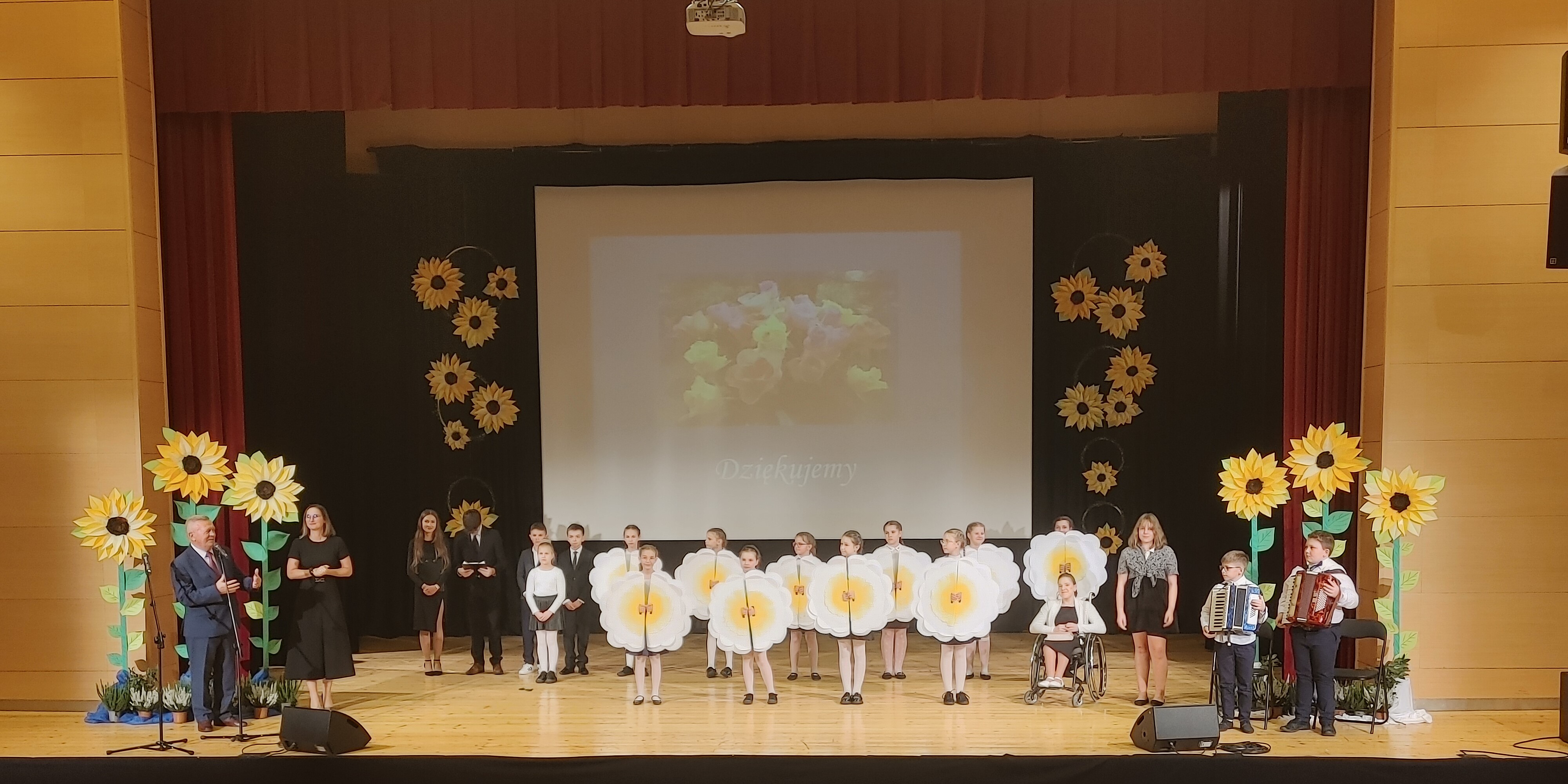 Zdjęcie przedstawia uczniów Szkoły Podstawowej Nr 1 stojących na scenie wraz z Wójtem Gminy Jabłonka i Dyrektorem Oświaty podczas Gminnych Obchodów Dnia Edukacji Narodowej.