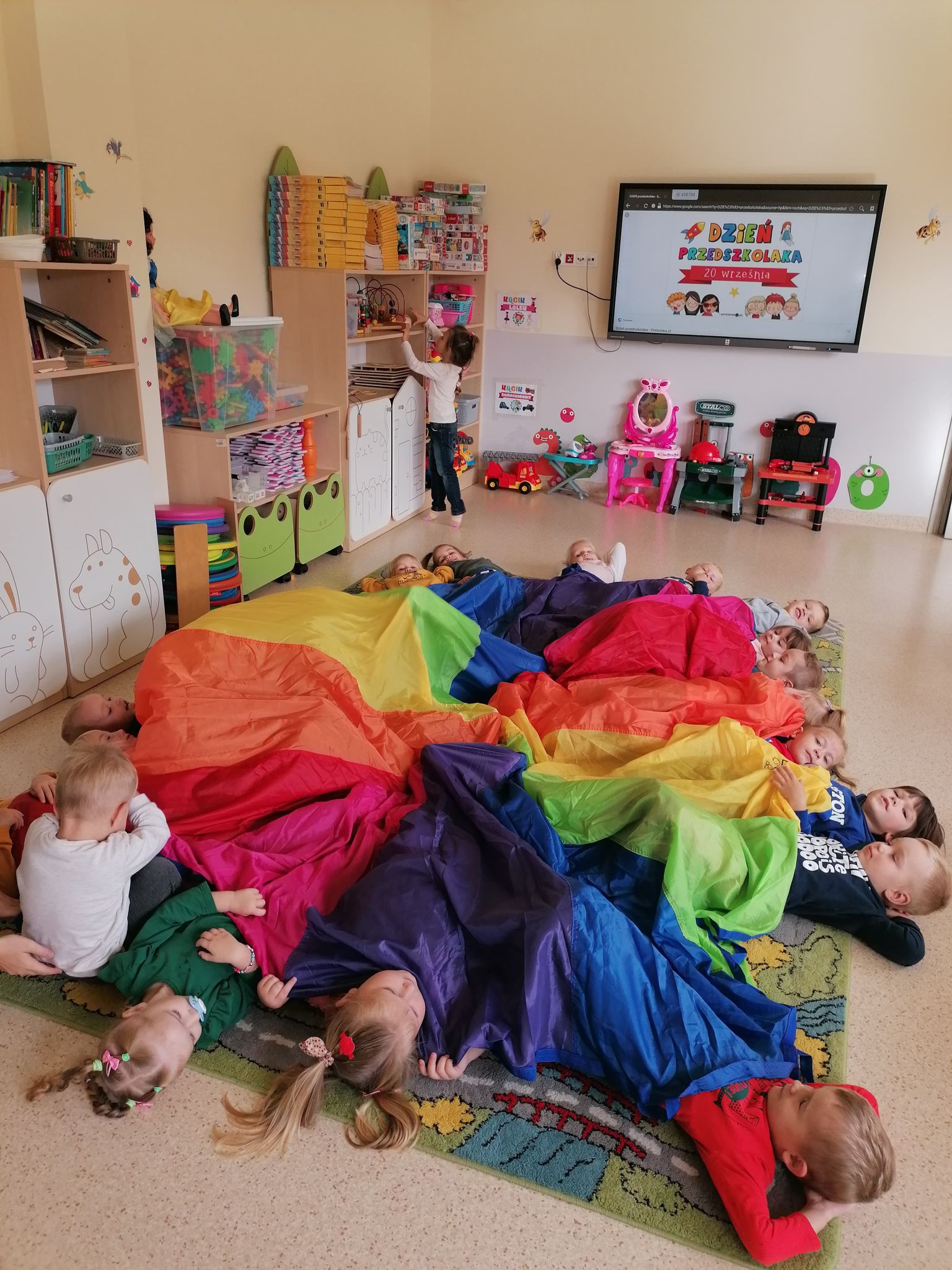 Zdjęcie przedstawia grupę uczniów oddziału przedszkolnego bawiących się na dywanie.
