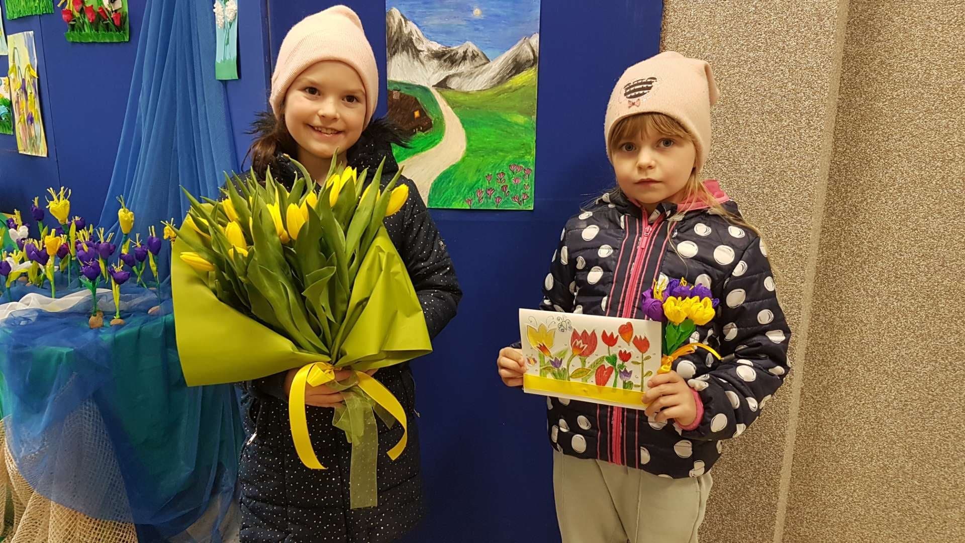 Zdjęcie przedstawia uczennice klasy pierwszej trzymające bukiet z żółtych tulipanów i kartkę z życzeniami dla Służby Zdrowia