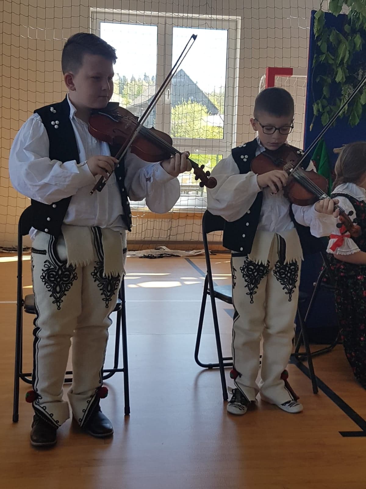 Zdjęcie przedstawia dwóch uczniów klasy drugiej w strojach orawskich, grających na skrzypcach.