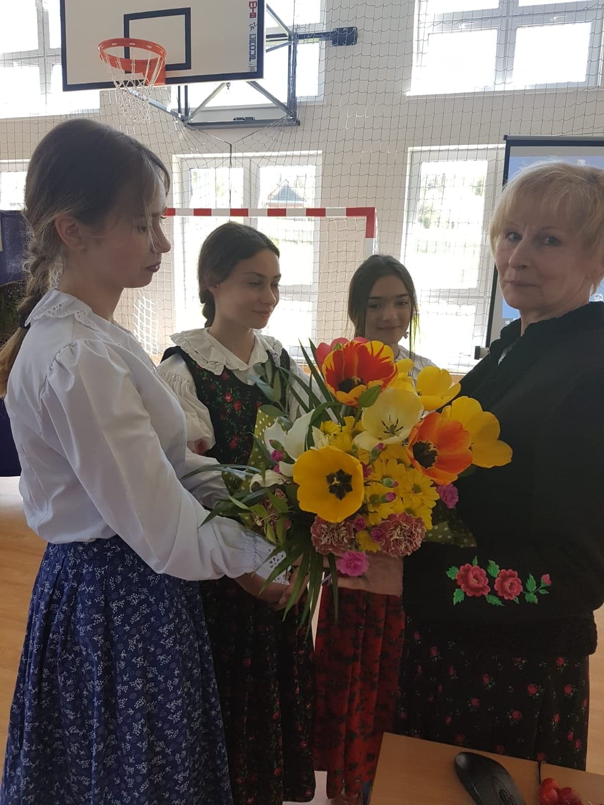 Zdjęcie przedstawia Panią Dyrektor Władysławę Omylak wraz z uczennicami wręczającymi bukiet kwiatów