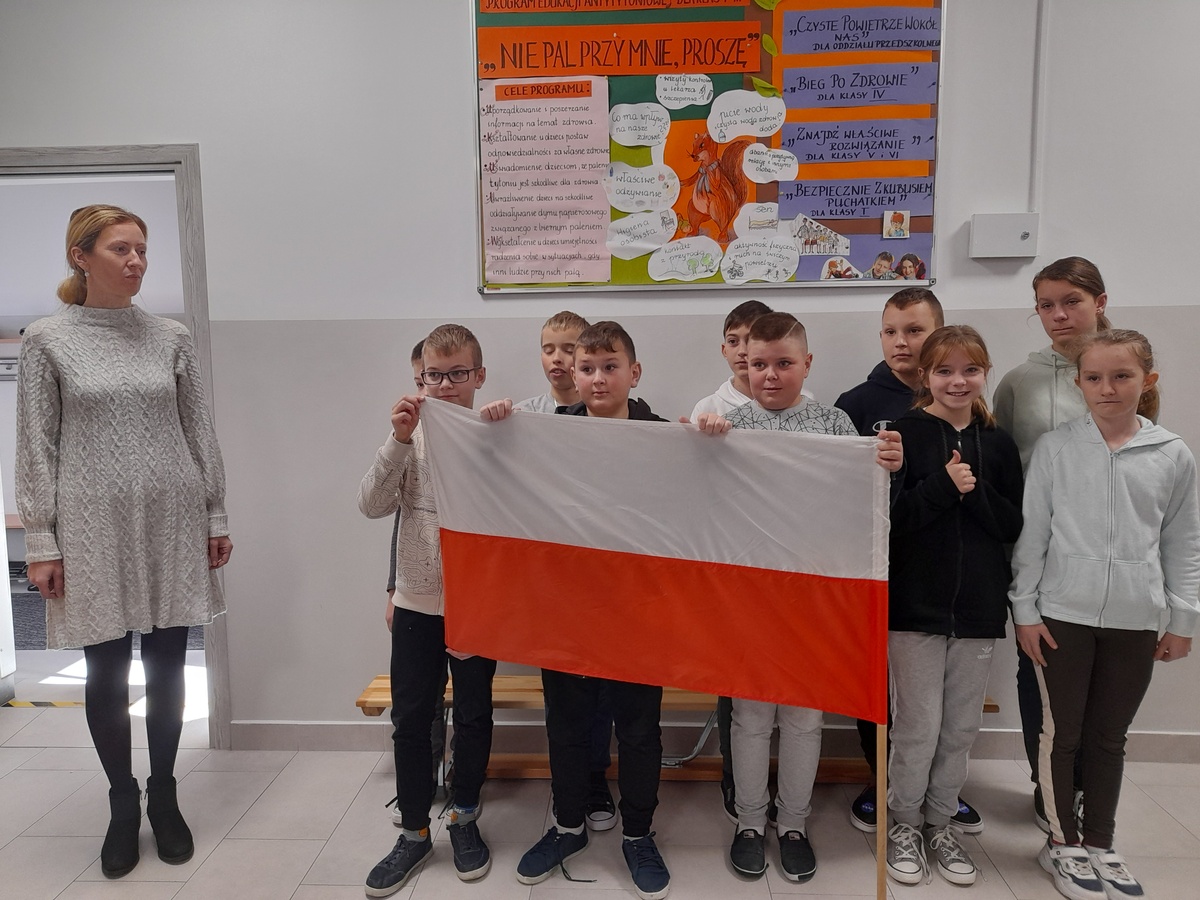 Grupa kilkunastu uczniów trzymających Flagę Polski wraz z nauczycielem