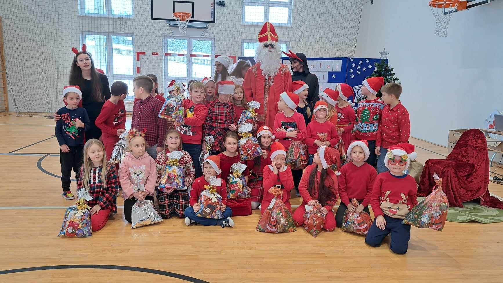 Zdjęcie przedstawia dzieci z prezentami i Mikołajem.