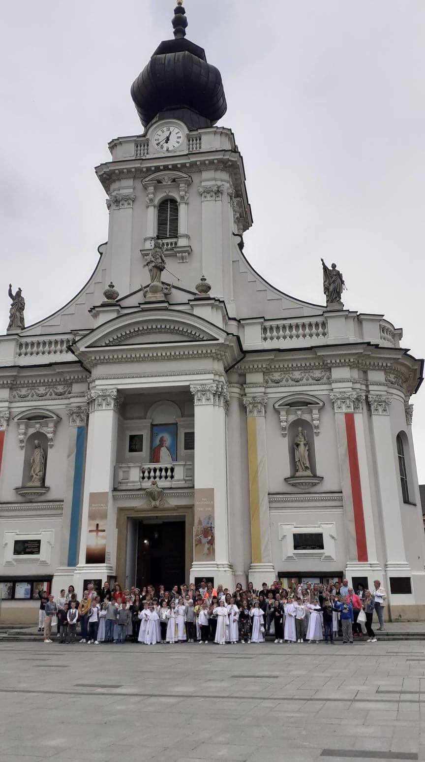 Zdjęcie przedstawia grupę uczniów wraz z rodzicami stojących przed Bazyliką Ofiarowania Najświętszej Maryi Panny w Wadowicach podczas pielgrzymki pokomunijnej