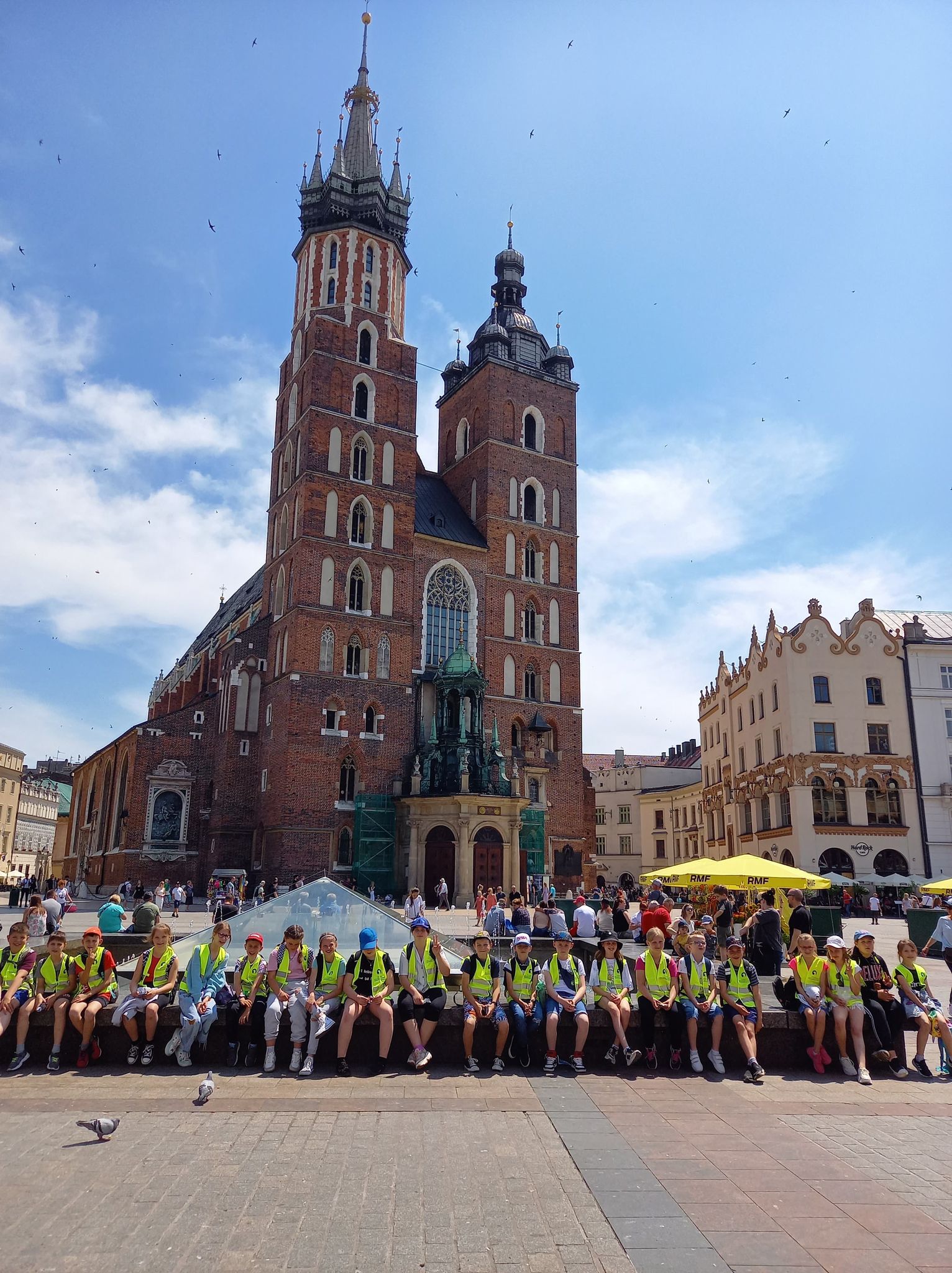 Zdjęcie uczniów klasy czwartej na rynku w Krakowie z widokiem na Bazylikę Mariacką.